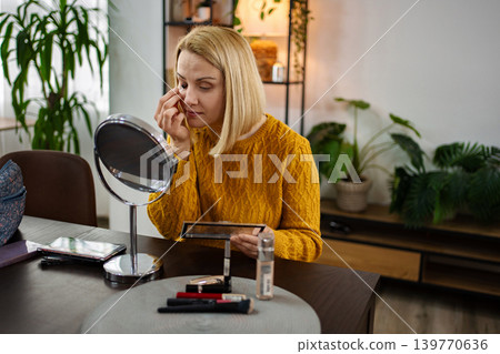 Woman applying makeup in a cozy, plant-filled room during the afternoon with soft light illuminating her focus and creativity Woman applying makeup in a cozy, plant-filled room during the afternoon with soft light illuminating her focus and creativity 139770636