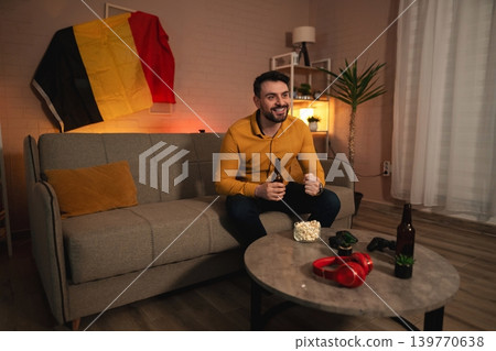 Excitement fills the room as a sports fan enjoys a cozy evening at home celebrating a game with snacks and drinks Excitement fills the room as a sports fan enjoys a cozy evening at home celebrating a game with snacks and drinks 139770638