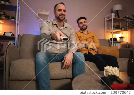 Friends enjoying an entertaining evening while watching a movie in a cozy living room filled with warm lighting 139770642