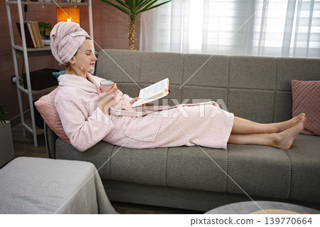 Woman relaxing on sofa with beauty mask, reading and drinking tea Woman relaxing on sofa with beauty mask, reading and drinking tea 139770664