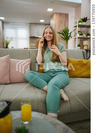 Soft-colored living room with a cheerful woman enjoying a phone call 139770950