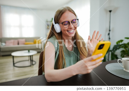 Smiling girl enjoying a video call while wearing headphones indoors 139770951