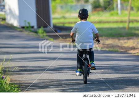 A boy's back as he practices riding a bicycle. A boy's back as he practices riding a bicycle. 139771041