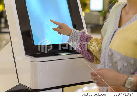 Close-up of a person's hand interacting with a digital touch screen on a modern white self-service kiosk, likely for check-in or service in a public place Close-up of a person's hand interacting with a digital touch screen on a modern white self-service kiosk, likely for check-in or service in a public place 139771384