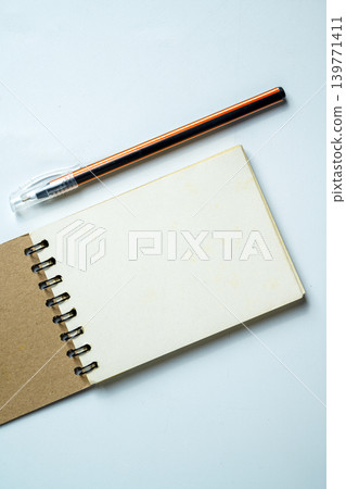 Top view of an open blank spiral notepad with an orange ballpoint pen on a neutral light-colored textured background, perfect for educational, business, or creative planning concepts Top view of an open blank spiral notepad with an orange ballpoint pen on a neutral light-colored textured background, perfect for educational, business, or creative planning concepts 139771411