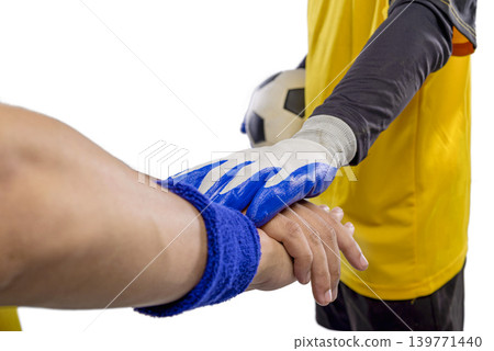 A close-up of soccer players stacking hands, showing teamwork and sportsmanship. One player wears goalkeeper gloves while holding a ball, symbolizing cooperation and readiness for a match 139771440