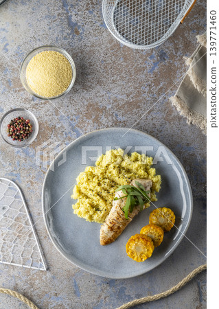 Grilled chicken breast with corn and aromatic couscous, ingredients and kitchen utensils surrounding plate Grilled chicken breast with corn and aromatic couscous, ingredients and kitchen utensils surrounding plate 139771460