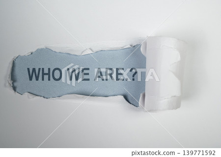 A creative concept image showing the phrase 'WHO WE ARE.?' revealed beneath a strip of torn white paper on a light blue background, representing identity and discovery A creative concept image showing the phrase 'WHO WE ARE.?' revealed beneath a strip of torn white paper on a light blue background, representing identity and discovery 139771592