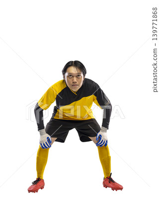 A young Indonesian southeast asian male soccer goalkeeper in a yellow and black uniform with gloves and red cleats, standing in a ready stance isolated on a white background 139771868