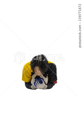 A Indonesian southeast asian goalkeeper in a yellow and black jersey lies face down on a soccer ball, clutching it with gloved hands. Isolated on a white background A Indonesian southeast asian goalkeeper in a yellow and black jersey lies face down on a soccer ball, clutching it with gloved hands. Isolated on a white background 139771872