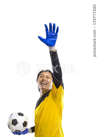 An enthusiastic Indonesian southeast asian soccer goalkeeper in a yellow jersey and blue gloves, holding a soccer ball and raising his hand in celebration, isolated on a white background An enthusiastic Indonesian southeast asian soccer goalkeeper in a yellow jersey and blue gloves, holding a soccer ball and raising his hand in celebration, isolated on a white background 139771880