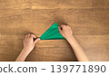 孩子的小手將綠色的摺紙折成三角形，就在角相接的那一刻。 139771890