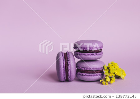 Three french macarons with yellow flowers on a purple background. Place for text. Three french macarons with yellow flowers on a purple background. Place for text. 139772143