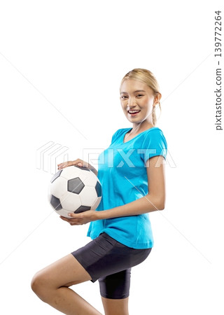 A beautiful young Indonesian southeast asian woman with blonde hair, wearing a blue t-shirt, poses while holding a classic black and white soccer ball near her face against a plain white background A beautiful young Indonesian southeast asian woman with blonde hair, wearing a blue t-shirt, poses while holding a classic black and white soccer ball near her face against a plain white background 139772264