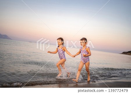 Happy twin sisters holding hands splashing in Greek sea Happy twin sisters holding hands splashing in Greek sea 139772479