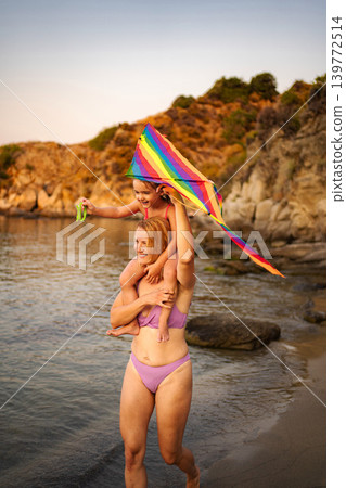 Mother carrying daughter on shoulders playing kite on beach Mother carrying daughter on shoulders playing kite on beach 139772514