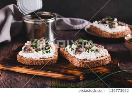 Delicious sandwiches on rye bread with ricotta, sardines and onions on a board on the table 139773022