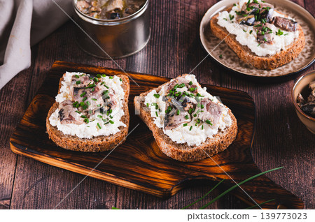 Slices of black bread with ricotta and sardines canned in oil on a board on a table 139773023