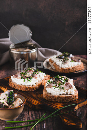 Delicious sandwiches on rye bread with ricotta, sardines and onions on a board vertical view 139773024