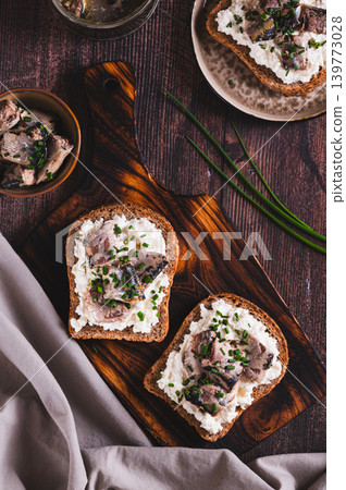Slices of black bread with ricotta and sardines canned in oil on a board on a table top and vertical view 139773028