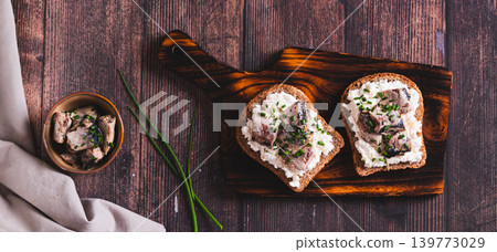 Slices of black bread with ricotta and sardines canned in oil on a board top view web banner 139773029
