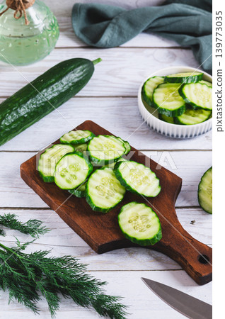 Slices of homegrown fresh cucumbers on a board and dill on a table vertical view Slices of homegrown fresh cucumbers on a board and dill on a table vertical view 139773035
