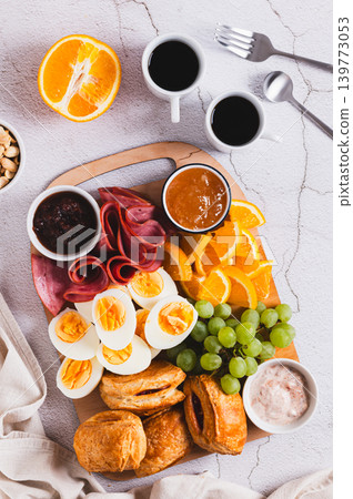 Boiled eggs, ham, buns, fruit and jam for breakfast on a board on the table top and vertical view 139773053