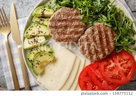 Low-carb burger with cheese, avocado, grilled patty, tomatoes and arugula close-up on a plate. Horizontal top view Low-carb burger with cheese, avocado, grilled patty, tomatoes and arugula close-up on a plate. Horizontal top view 139773112