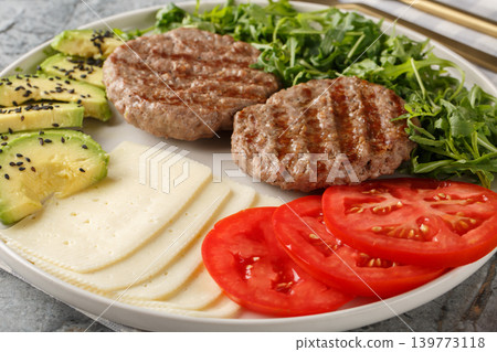 Low-carb burger with cheese, avocado, grilled patty, tomatoes and arugula close-up on a plate. Horizontal Low-carb burger with cheese, avocado, grilled patty, tomatoes and arugula close-up on a plate. Horizontal 139773118