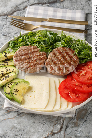 Diet beef burger with cheese, avocado, grilled patty, tomatoes and arugula close-up on a plate. Vertical Diet beef burger with cheese, avocado, grilled patty, tomatoes and arugula close-up on a plate. Vertical 139773119