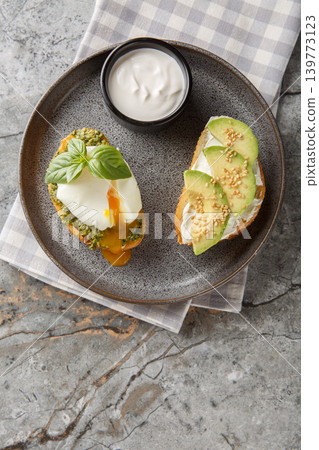 Low-carb toast with poached egg and basil pesto, as well as with avocado and cream cheese close-up on a plate. Vertical top view Low-carb toast with poached egg and basil pesto, as well as with avocado and cream cheese close-up on a plate. Vertical top view 139773123