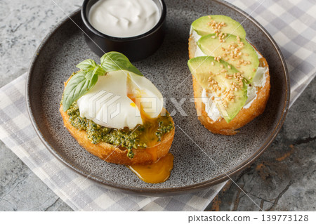 Keto breakfast toast with poached egg and basil pesto, avocado, and cream cheese, close-up on a plate. Horizontal Keto breakfast toast with poached egg and basil pesto, avocado, and cream cheese, close-up on a plate. Horizontal 139773128