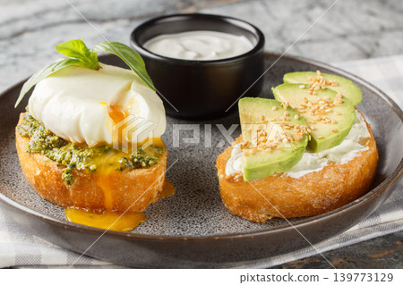 Low-carb toast with poached egg and basil pesto, as well as with avocado and cream cheese close-up on a plate. Horizontal Low-carb toast with poached egg and basil pesto, as well as with avocado and cream cheese close-up on a plate. Horizontal 139773129