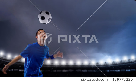 Professional Indonesian southeast asian soccer player in a blue jersey looks up to head a football during a match in a large stadium at night illuminated by bright floodlights Professional Indonesian southeast asian soccer player in a blue jersey looks up to head a football during a match in a large stadium at night illuminated by bright floodlights 139773220