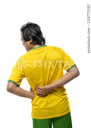 A Indonesian southeast asian man in a yellow and green sports uniform holding his lower back in pain, suggesting a sports injury or muscle strain, isolated on a white background A Indonesian southeast asian man in a yellow and green sports uniform holding his lower back in pain, suggesting a sports injury or muscle strain, isolated on a white background 139773262