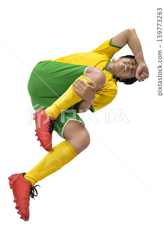 Young Indonesian southeast asian soccer player in a yellow and green uniform lying on the ground, grimacing and clutching his knee after a sports injury. Full body shot isolated on a white background Young Indonesian southeast asian soccer player in a yellow and green uniform lying on the ground, grimacing and clutching his knee after a sports injury. Full body shot isolated on a white background 139773263