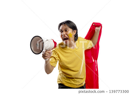 Enthusiastic Indonesian southeast asian sports supporter with face paint shouting into a megaphone and holding a red flag. Isolated on a white background, representing passion and team spirit 139773300