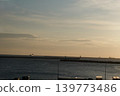 A scene of a distant cargo ship and breakwater floating on the calm sea before sunrise. 139773486
