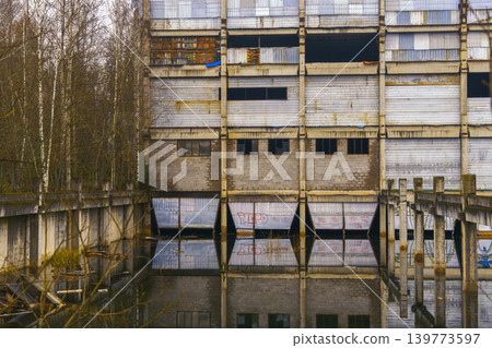 Mirror water decay. Serene water mirrors old industrial site with broken roofs and surrounding trees 139773597