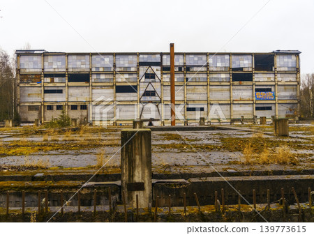Desolate urban scene. Derelict concrete lot leading to forgotten multi level building under cloudy dreary sky Desolate urban scene. Derelict concrete lot leading to forgotten multi level building under cloudy dreary sky 139773615