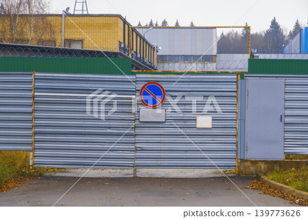 Corrugated metal barrier displaying parking warnings and small pedestrian entrance in worn urban setting Corrugated metal barrier displaying parking warnings and small pedestrian entrance in worn urban setting 139773626