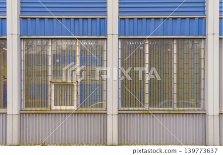 Robust factory facade. Utilitarian industrial exterior highlighted by reinforced frames and bars Robust factory facade. Utilitarian industrial exterior highlighted by reinforced frames and bars 139773637