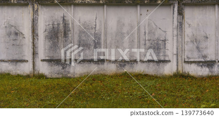 Weathered concrete with moss. Worn concrete fence featuring moss stains and grassy foreground landscape 139773640