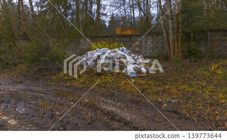 Illegal debris disposal site with plastic and insulation scattered across wet terrain near trees Illegal debris disposal site with plastic and insulation scattered across wet terrain near trees 139773644