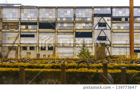 Old empty building overtaken by nature. Neglected city block featuring broken windows and overgrown fences 139773647