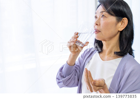 Senior woman taking medicine by the window Senior woman taking medicine by the window 139773835