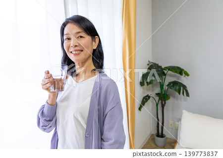 A senior woman drinking water by the window. A senior woman drinking water by the window. 139773837