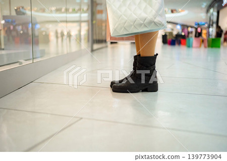 Shopper standing in mall aisle wearing black boots Shopper standing in mall aisle wearing black boots 139773904