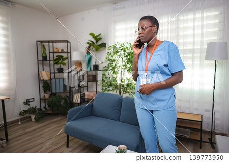 Nurse wearing blue scrubs talking on phone in bright living room Nurse wearing blue scrubs talking on phone in bright living room 139773950