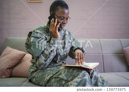 Smiling african american soldier talking on smartphone and reading book at home 139773975